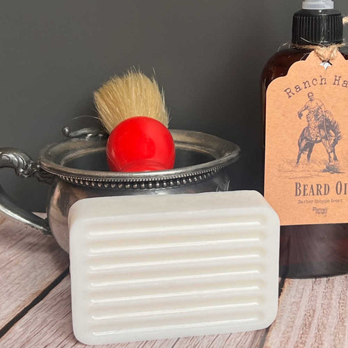 Bar of soap, brush, and bottle of beard oil on a wooden surface with a dark background