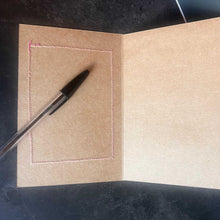 Brown paper  card with a pen on a dark surface has stitching 