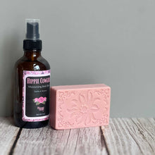 Bottle of Hippie Cowgirl body wash and pink soap bar on a wooden surface with a gray background
