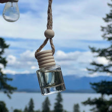 Glass bottle with wooden cap hanging against a scenic background of trees and water.