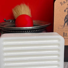 White bar of soap with a red object and brush in the background on a red surface.